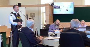 Man in OPP uniform stands at a microphone in front of councillors.