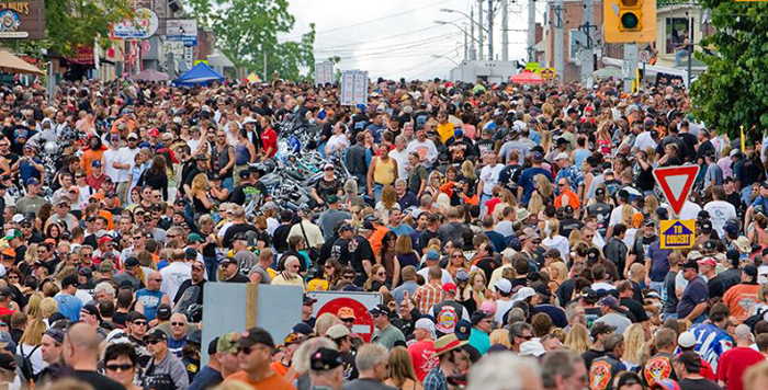 A large crowd of pedestrians and parked motorcycles fill Main Street.