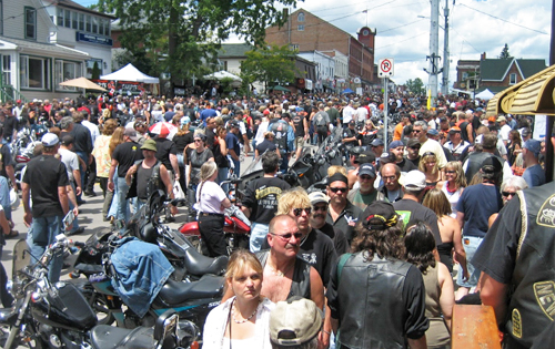 A large crowd of pedestrians and parked motorcycles fill Main Street.
