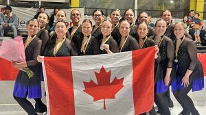 A group of women skaters wearing medals around their necks stand on the ice with a Canadian flag