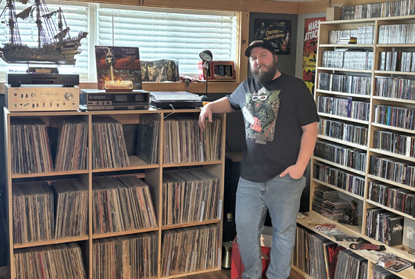 Man stands in front of bookshelves full of vinyl records and CDs
